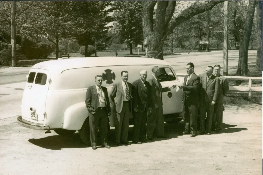 Historic image of a white ambulance with several men standing in front of it